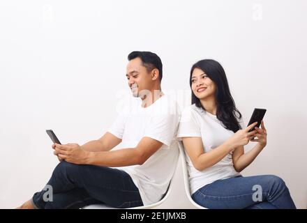 Glücklich asiatische paar sitzen während halten ihre Smartphone. Isolierter o weißer Hintergrund Stockfoto