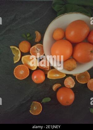 Ganze und geschnittene Orangen auf einem luxuriösen dunklen Hintergrund unter Das Sonnenlicht Stockfoto
