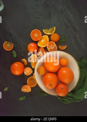 Ganze und geschnittene Orangen auf einem luxuriösen dunklen Hintergrund unter Das Sonnenlicht Stockfoto