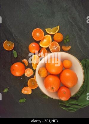 Ganze und geschnittene Orangen auf einem luxuriösen dunklen Hintergrund unter Das Sonnenlicht Stockfoto