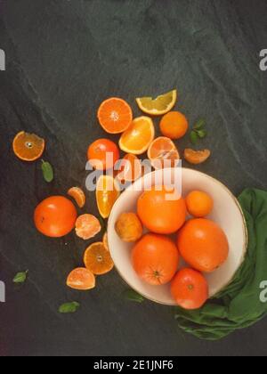 Ganze und geschnittene Orangen auf einem luxuriösen dunklen Hintergrund unter Das Sonnenlicht Stockfoto