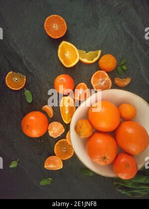 Ganze und geschnittene Orangen auf einem luxuriösen dunklen Hintergrund unter Das Sonnenlicht Stockfoto