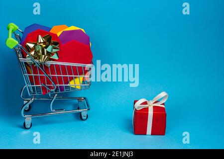 Rotes Geschenk mit weißem Band und Trolley mit Einkäufen auf Blauer Hintergrund Stockfoto