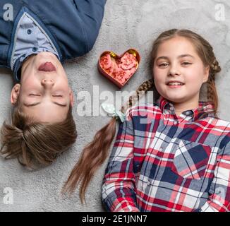 Lustige Schwester und Bruder halten Zungen aneinander, glückliche und lächelnde Teenager mit herzförmigen Keksen Stockfoto