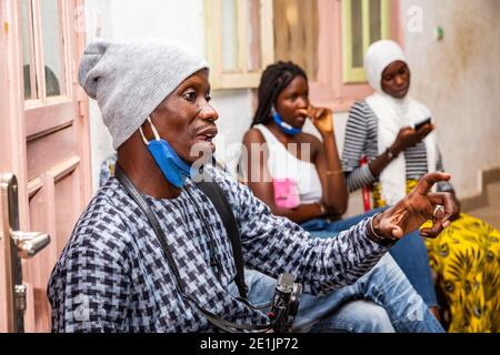 MBOUR, SENEGAL - DEZEMBER circa, 2020. Konzept zeigt die falsche Art der Verwendung von Gesichtsmasken während Coronavirus oder covid-19 Krise - junger schwarzer Mann wea Stockfoto