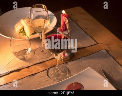Rotweinglas mit Weißweinglas auf rustikalem Trattoria Tisch Set mit roter Kerze im Kerzenständer, Textraum Stockfoto