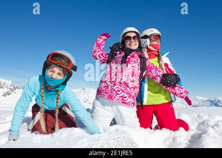Drei Teenager-Mädchen im Winterurlaub in den Bergen sitzen im frischen Schnee Blick auf die Kamera. Landschaft mit großem blauen Himmel und bunten Kleidern Stockfoto