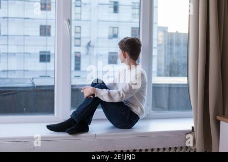 Der Junge sitzt auf der Fensterbank und schaut auf die Angezeigt Stockfoto