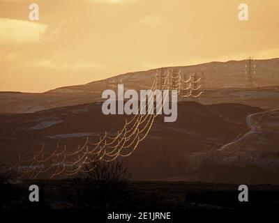 Das abendliche Sonnenlicht auf Hochspannungskabeln, die von Pylonen unterstützt werden, erstreckt sich wie goldene Spinnennetze in die entfernten Cumbrian-Hügel - England, Großbritannien Stockfoto