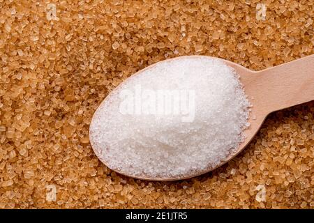 Holzlöffel voll mit raffiniertem Granulatzucker auf braunem Granulatzucker. Stockfoto