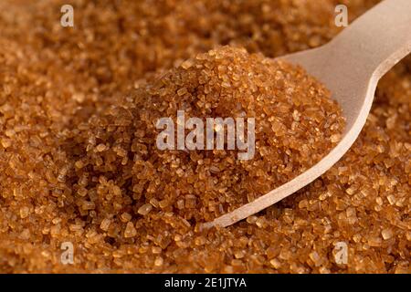 Holzlöffel voll dunkelbraunem Granulatzucker auf braunem Granulatzucker. Stockfoto