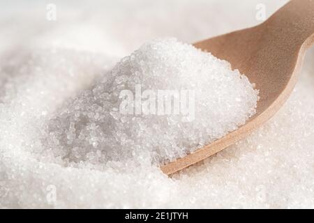 Holzlöffel voll raffiniertem Granulatzucker auf raffiniertem Granulatzucker. Stockfoto