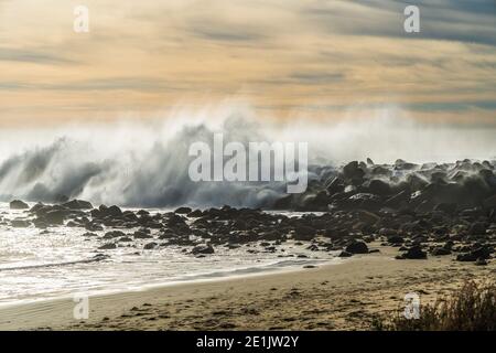 Felsiger Sonnenuntergang am Strand und stürmische Meereswellen, die hoch in die Luft gegen Felsen in Morro Bay, Central California Coast, plätschern Stockfoto