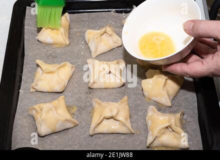 Vor dem Backen im Ofen Eigelb auf Blätterteighüllen abschmieren. Nahaufnahme. Speicherplatz kopieren. Stockfoto