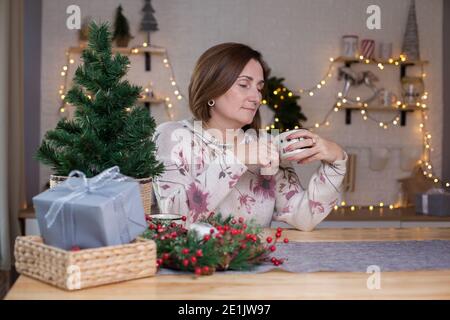 Frau, die an einem Tisch sitzt und heiße Schokolade trinkt weihnachtlich dekoriertes Zimmer Stockfoto