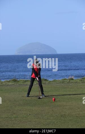 Städtischer Golfplatz Girvan, Ayrshire, Schottland, Großbritannien. Golferin auf dem ersten T-Shirt mit Ailsa Craig im Hintergrund Stockfoto