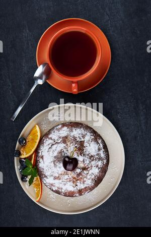 Köstlicher fruchtiger Kuchen in Teller mit Scheiben getrockneter Orange und einer Tasse Tee auf dunklem Tischhintergrund, Nahaufnahme, Draufsicht Stockfoto