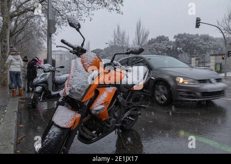 Madrid, Spanien - 07. Januar 2021: Ein orangefarbenes Motorrad, schneebedeckt, und Verkehr auf der Avenida de Menedez Pelayo, mitten in einer Welle von Pol Stockfoto