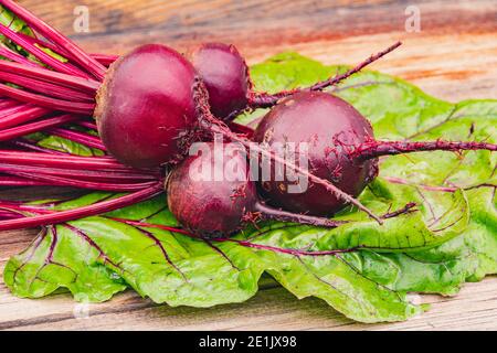 Rote Bete Knollen mit grünen Blättern auf Holztisch. Zubereitung von frischem Salat. Frisches Gemüse für vegetarische Küche. Rüben auf dem Straßenmarkt. Stockfoto