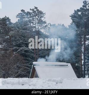 Rauch aus dem Kamin auf dem schneebedeckten Dach des Hauses Stockfoto