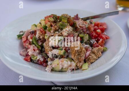 Gesunder griechischer Salat, frisches Gemüse mit Tomaten, Pfeffer, Gurken, roten Zwiebeln, Oliven, Feta-Käse in Teller auf dem Tisch. Spezialität der isla Stockfoto