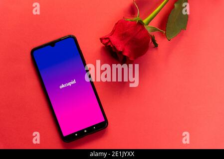 London, UK - 6. januar 2021: okcupid Dating App-Logo auf dem Handy mit Gesichtsmaske und roter Rose. Konzept der Online-Suche nach Partnern. Romantische Wohnung Stockfoto