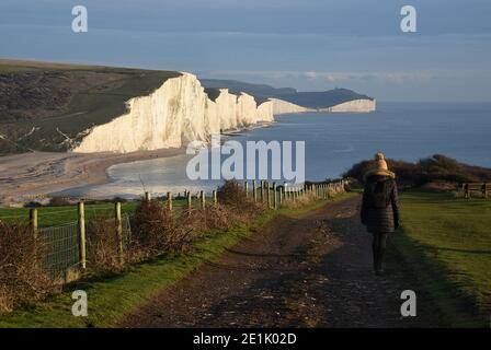 Einsame Frau, die im Winter auf dem Küstenweg zu den majestätischen weißen Klippen der Seven Sisters in der Nähe von Seaford, Sussex, England, Großbritannien, wandert Stockfoto