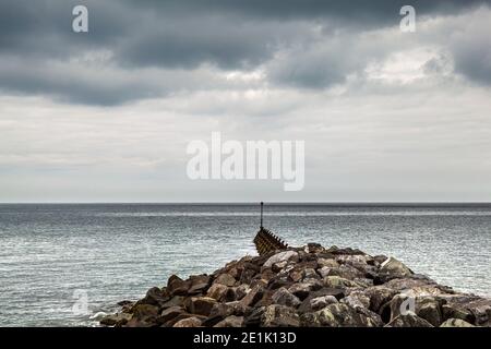 Blick auf das Meer an einem bewölkten Tag vorbei an der Hafenverteidigung von Aberaeron, Ceredigion, Wales Stockfoto