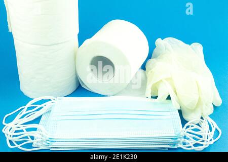 Rollen Toilettenpapier und eine medizinische Maske auf blauem Hintergrund. Weiße Toilettenpapierrolle und blaue Gesichtsmaske. Das Konzept des Wesentlichen während einer Pandemie Stockfoto
