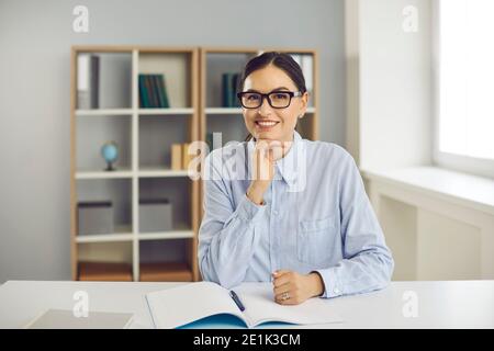 Glückliche junge Lehrer oder College-Student am Schreibtisch sitzen Und lächelnd auf die Kamera Stockfoto