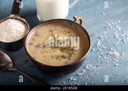 Pilzsahnesuppe in Schüssel mit Glas Milch auf Holzgrund. Stockfoto