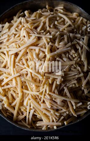 Schüssel mit traditionellen türkischen Nudeln (roh) mit Eiern auf dunklem Hintergrund. Türkische Stil inländische handgemachte Nudel (eriste) auf Holzhintergrund. Stockfoto