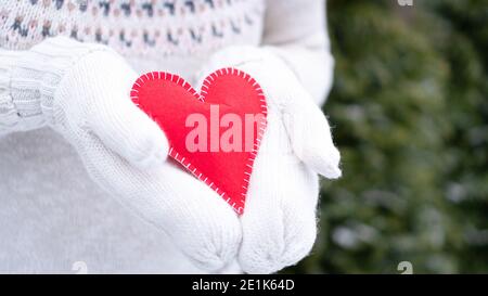 Liebe Deklaration Konzept. Liebe als Geschenk. Das Konzept der Gefühle und Emotionen am Valentinstag. Ein Mädchen in einem weißen Strickpullover und Fäustlinge hält Stockfoto