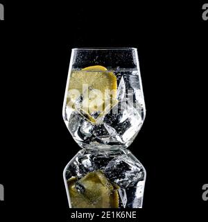 Gin Tonic mit Eiswürfeln und Zitronenscheibe In Glas auf schwarzem Hintergrund Stockfoto