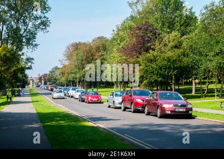 Autos an einem hellen sonnigen Tag mit einem Auto geparkt Fahren Sie vorbei an der von Bäumen gesäumten Haupteinfahrt nach Stanley Park Blackpool Lancashire England Großbritannien Stockfoto