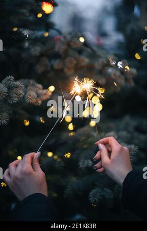 Die Hand der Frau hält Wunderkerzen auf dem Hintergrund eines Weihnachtsfestes Baum mit Lichtern Stockfoto