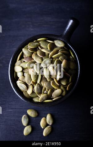 Rohe Kürbiskerne in schwarzer Keramikschale auf dunklem Hintergrund. Stockfoto