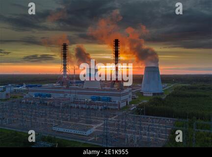 Dampf aus den Kühltürmen des Kraftwerks. Ein Blick auf die Kraftwerksrohre bei Sonnenuntergang. Stockfoto