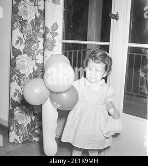 1950er niedliche Mädchen Kleinkind spielt mit Geburtstag Ballons, USA Stockfoto