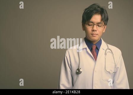 Junge gutaussehende asiatische Mann Arzt trägt Brillen vor grauem Hintergrund Stockfoto