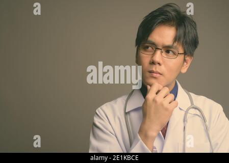 Junge gutaussehende asiatische Mann Arzt trägt Brillen vor grauem Hintergrund Stockfoto
