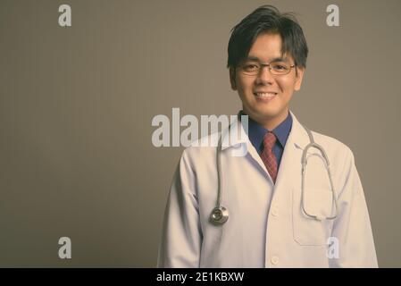 Junge gutaussehende asiatische Mann Arzt trägt Brillen vor grauem Hintergrund Stockfoto
