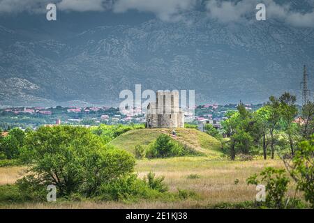 Sandstein St. Nikolaus Kirche mit Dinarischen Alpen im Hintergrund, ist römisch-katholische Kirche zwischen Zaton und Nin in Kroatien Stockfoto