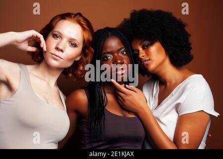 Junge hübsche kaukasische, afro, skandinavische Frau posiert fröhlich zusammen auf braunem Hintergrund, Lifestyle diverse Nationalität Menschen Konzept Stockfoto