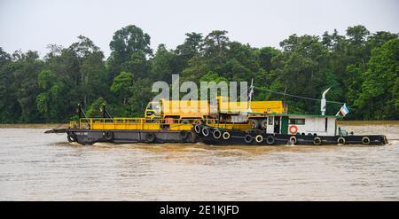 Schleppboot schiebt einen Lastkahn mit einem großen gelben Loch LKW den Kinabatangan Fluss hinunter Stockfoto