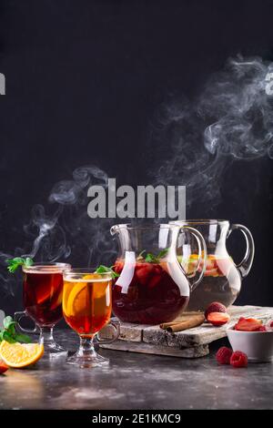 Auf dem Tisch zwei Krüge mit Limonade, Glühwein und mit Getränken gefüllte Gläser. Aus Getränken entsteht Dampf. Erdbeeren, Apeltsins, Himbeeren und Stockfoto