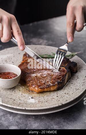 Person schneidet saftig gegrilltes rotes Rindfleisch Schweinefleisch Grillsteak Filet mit Rosmarinzweig Stockfoto