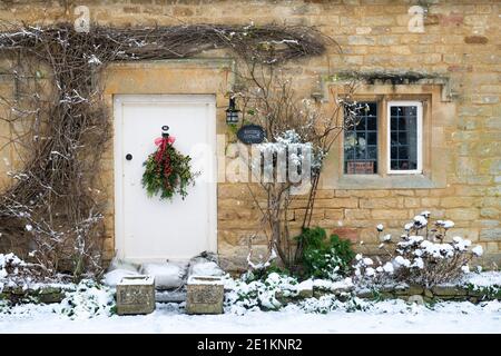Cotswold Steinhaus mit weihnachtskranz im Dezember Schnee. Taynton, Cotswolds, Oxfordshire, England Stockfoto