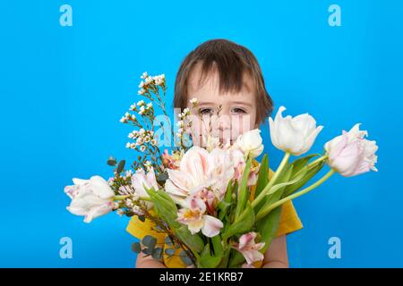 Niedlichen Jungen lächeln mit einem Blumenstrauß Tulpe Blumen als Ein Geschenk auf blauem Hintergrund im Studio Stockfoto