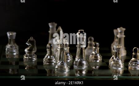 Schachfiguren aus Glas an Bord im Dunkeln Stockfoto